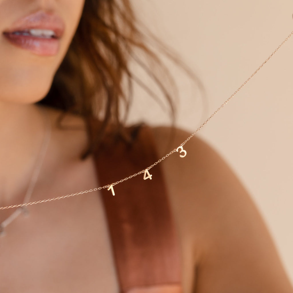 A woman wears the Alice Spaced Number Necklace with 1 4 3 gold charms, giving a minimalist accent to her look.