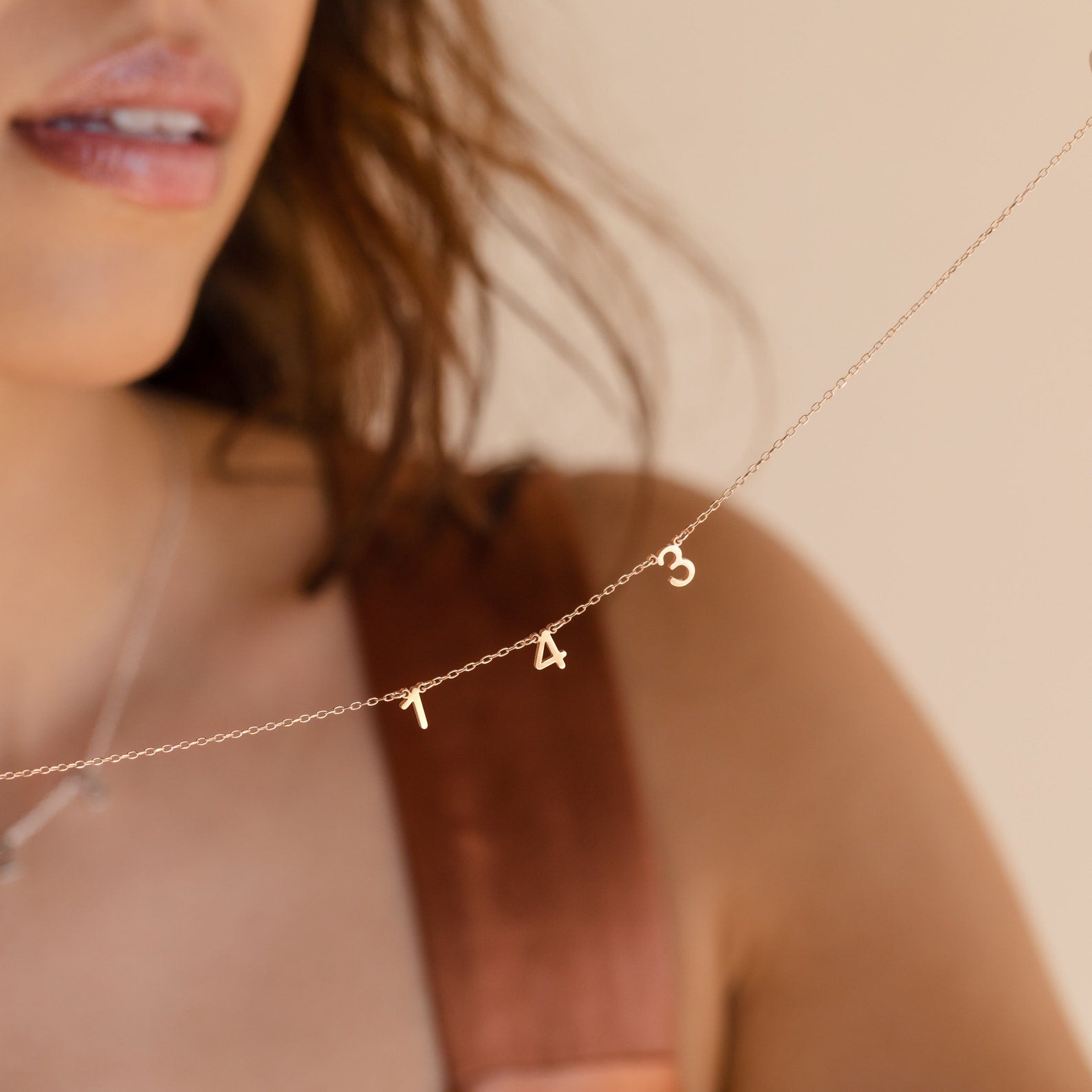 A woman wears the Alice Spaced Number Necklace with 1 4 3 gold charms, giving a minimalist accent to her look.