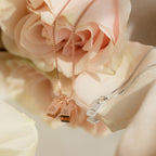 The Old English Mini Tag Necklace features gold or silver initial pendants on delicate chains, artfully displayed on pale pink rose petals—an ideal personalized gift.