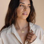 Woman wearing a cream shirt and the Old English Mini Tag Necklace with three rectangular gold pendants, looking off to the side.
