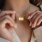 A woman holds the Carrie Mini Tag Necklace—a minimalist, personalized piece featuring three engraved letter pendants: B, A, and L.