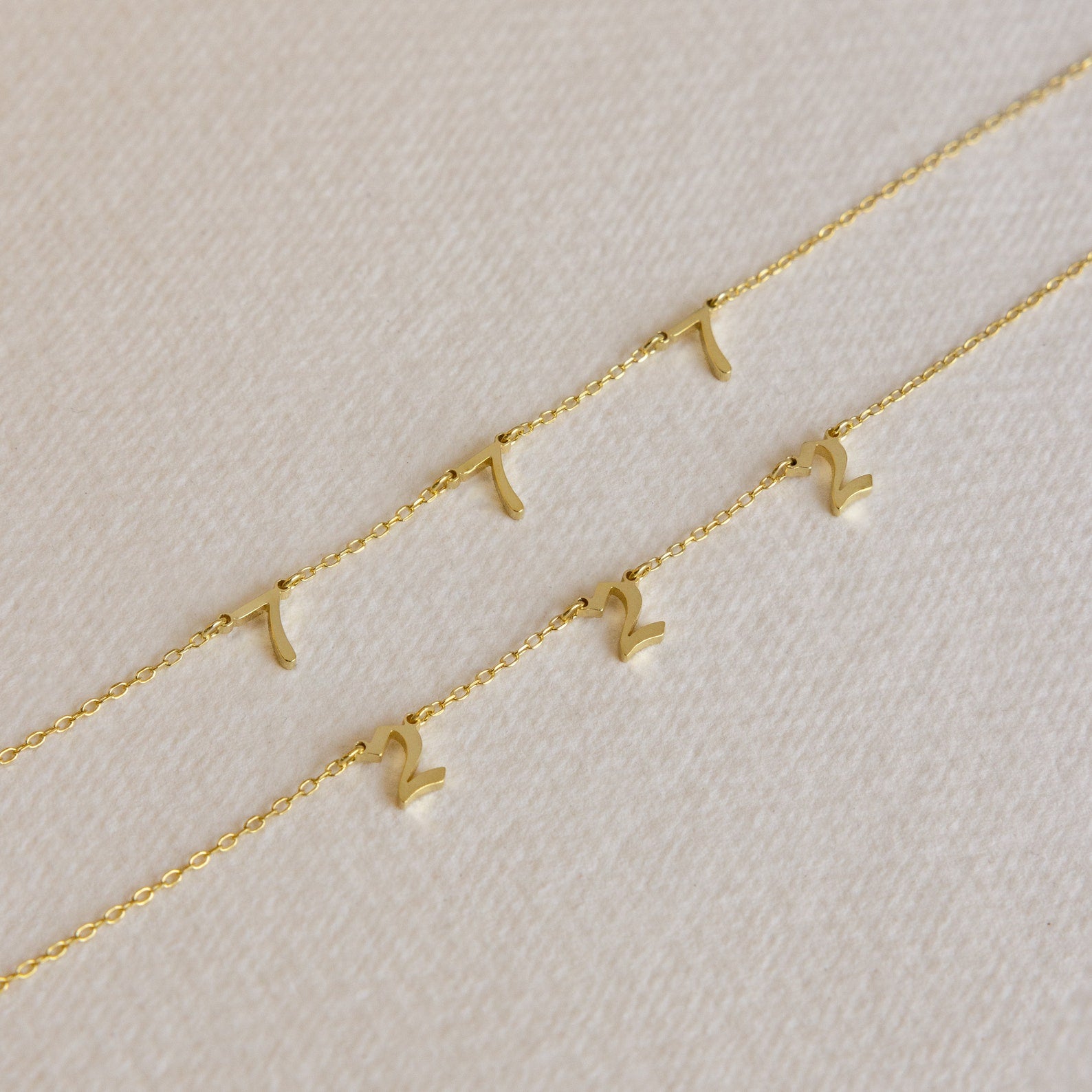Three Old English Spaced Number Necklaces with gold chains and small gold number “1” and “2” pendants displayed on a textured surface, highlighting a personalized vintage charm jewelry style.
