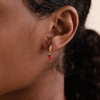 Close-up of a model wearing a gold huggie earring with a deep red baguette-cut garnet charm.
