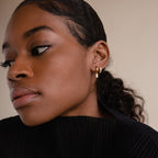 Model wearing two earrings—gold opal baguette huggie and a opal gold hoop—styled with a sleek ponytail and black top.