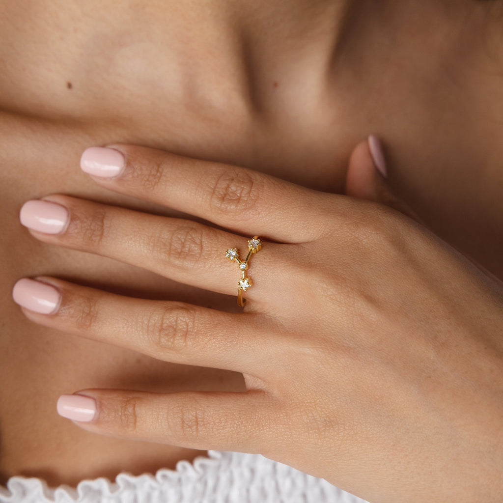 A hand with light pink nails wears the Constellation Ring on the ring finger, showcasing gold and small star-shaped accents for a celestial jewelry style.