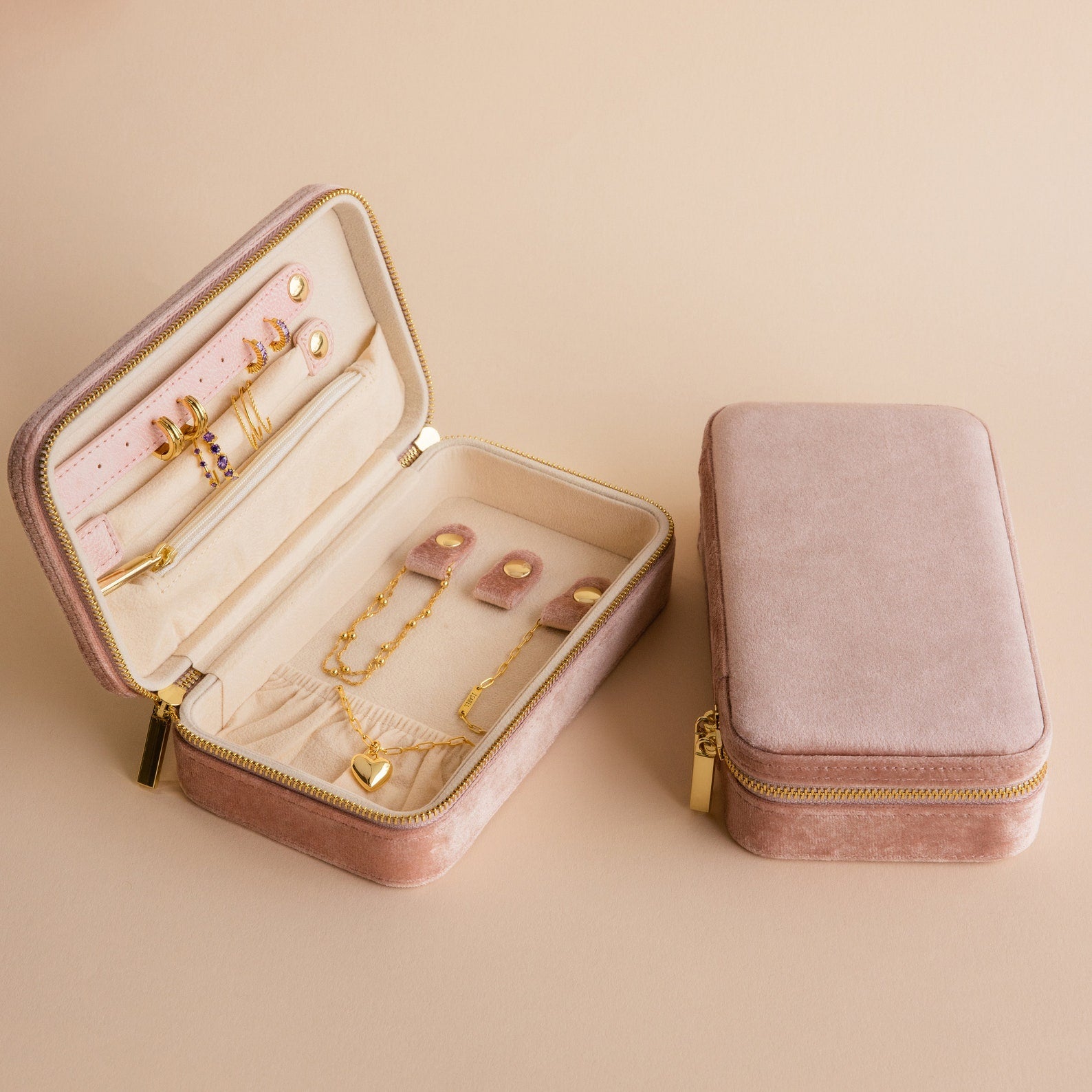The Rectangle Velvet Jewelry Case in pink velvet opens to reveal assorted gold jewelry, with a matching closed case beside it on a beige surface—a stylish organizer for your treasured pieces.