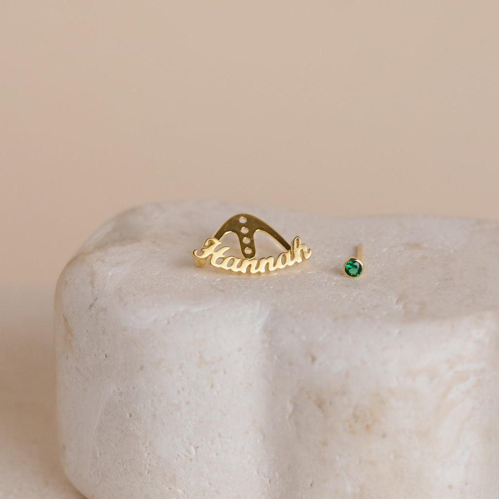The London Name Ear Jackets feature a gold "Hannah" pin on beige stone and a small gold stud with green gemstone—ideal for fans of personalized name or custom birthstone earrings.