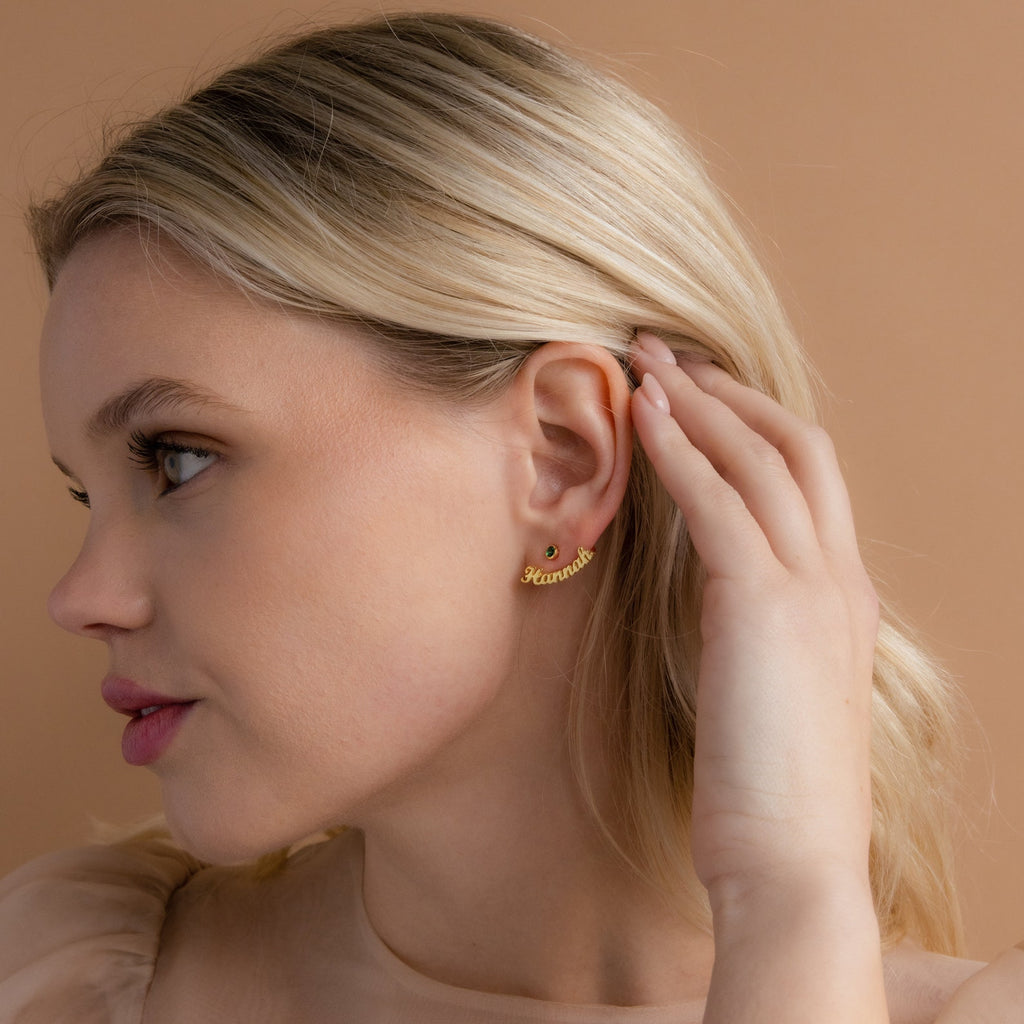 A blonde woman touches her ear, wearing London Name Ear Jackets personalized with "Rihanna," set against a beige background.
