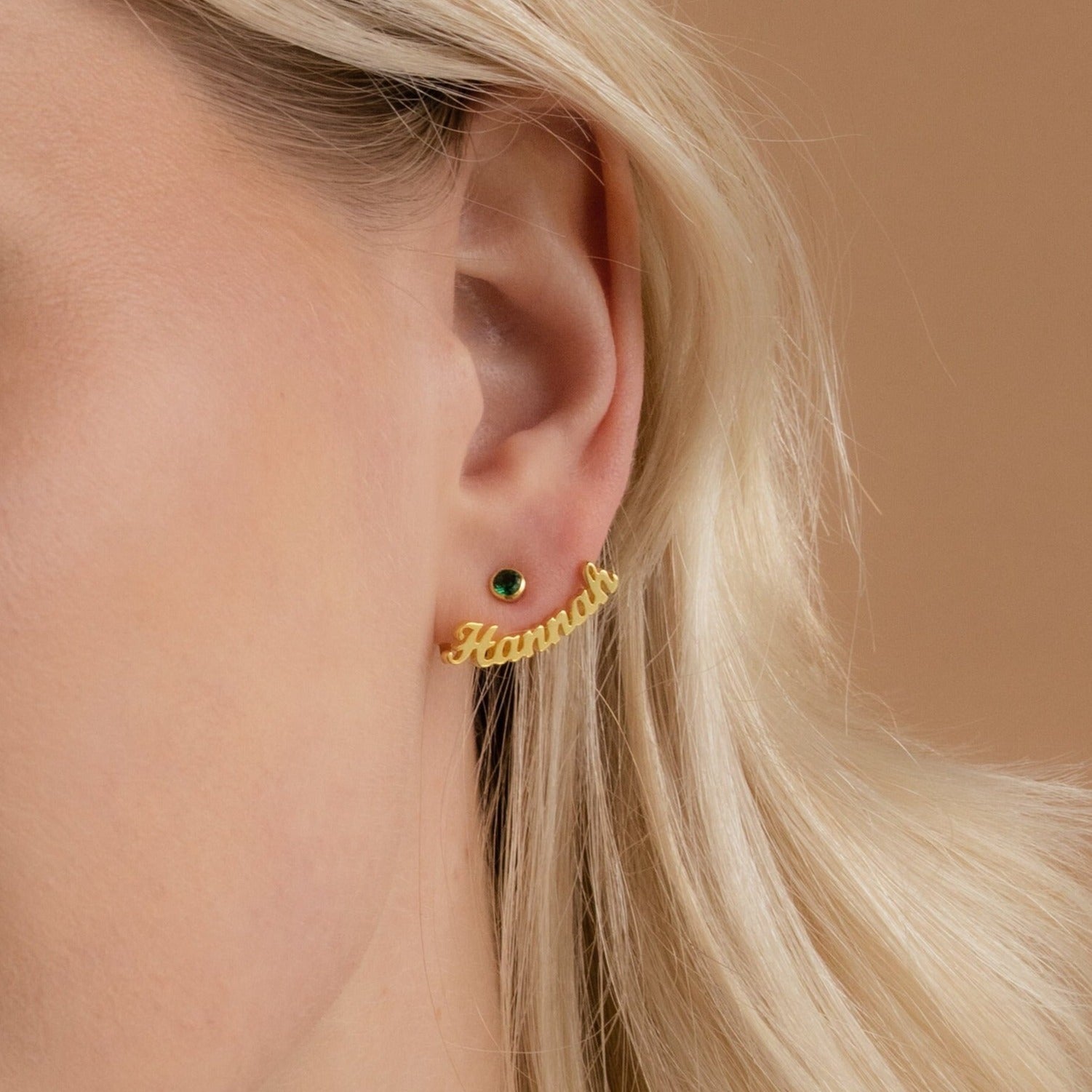 Close-up of an ear wearing a gold stud and London Name Ear Jackets, personalized in cursive to spell Hannah.