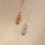Two Newsletter Oval Tag Necklaces, each featuring an engraved letter and a star-shaped birthstone, rest on a textured surface.