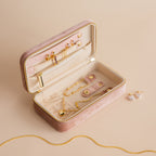 A Rectangle Velvet Jewelry Case in pink velvet displays gold necklaces, rings, and earrings on a beige surface.