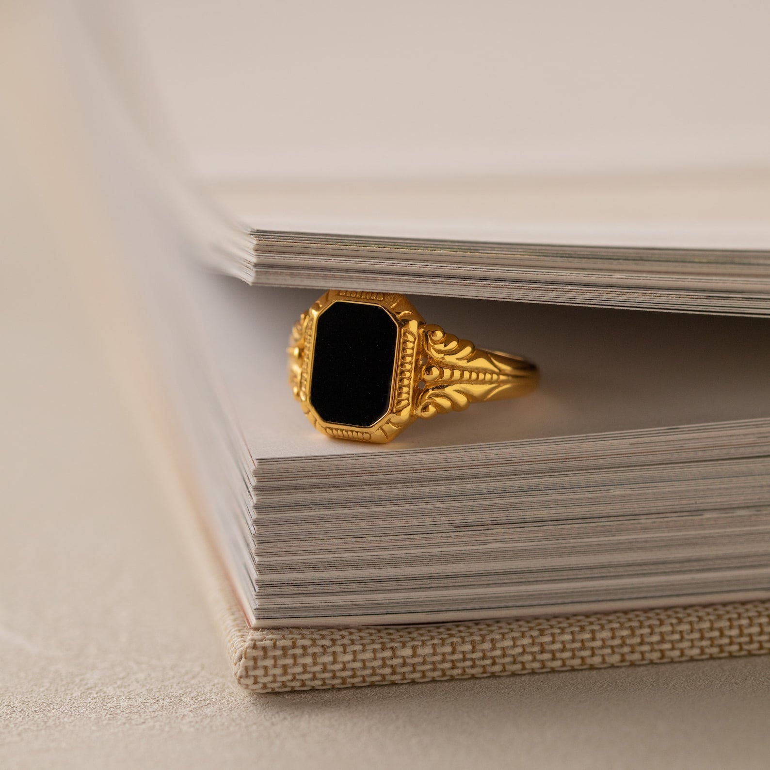 The Vintage Black Signet Ring, featuring a bold rectangular black stone, is displayed on the corner of an open book.