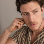 A man wearing a Vintage Black Signet Ring touches his ear while looking to the side, dressed in a beige striped shirt.