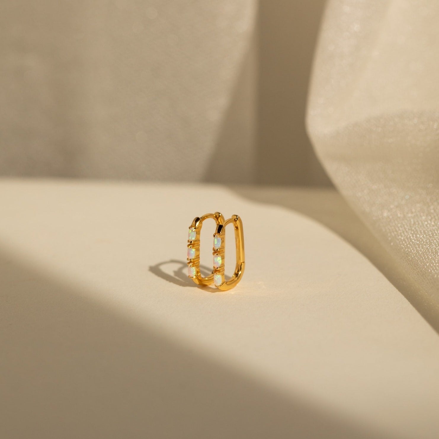 The Halo Opal Hoops, featured on a white surface, are perfect to pair with minimalist earrings for an elegant, refined look.