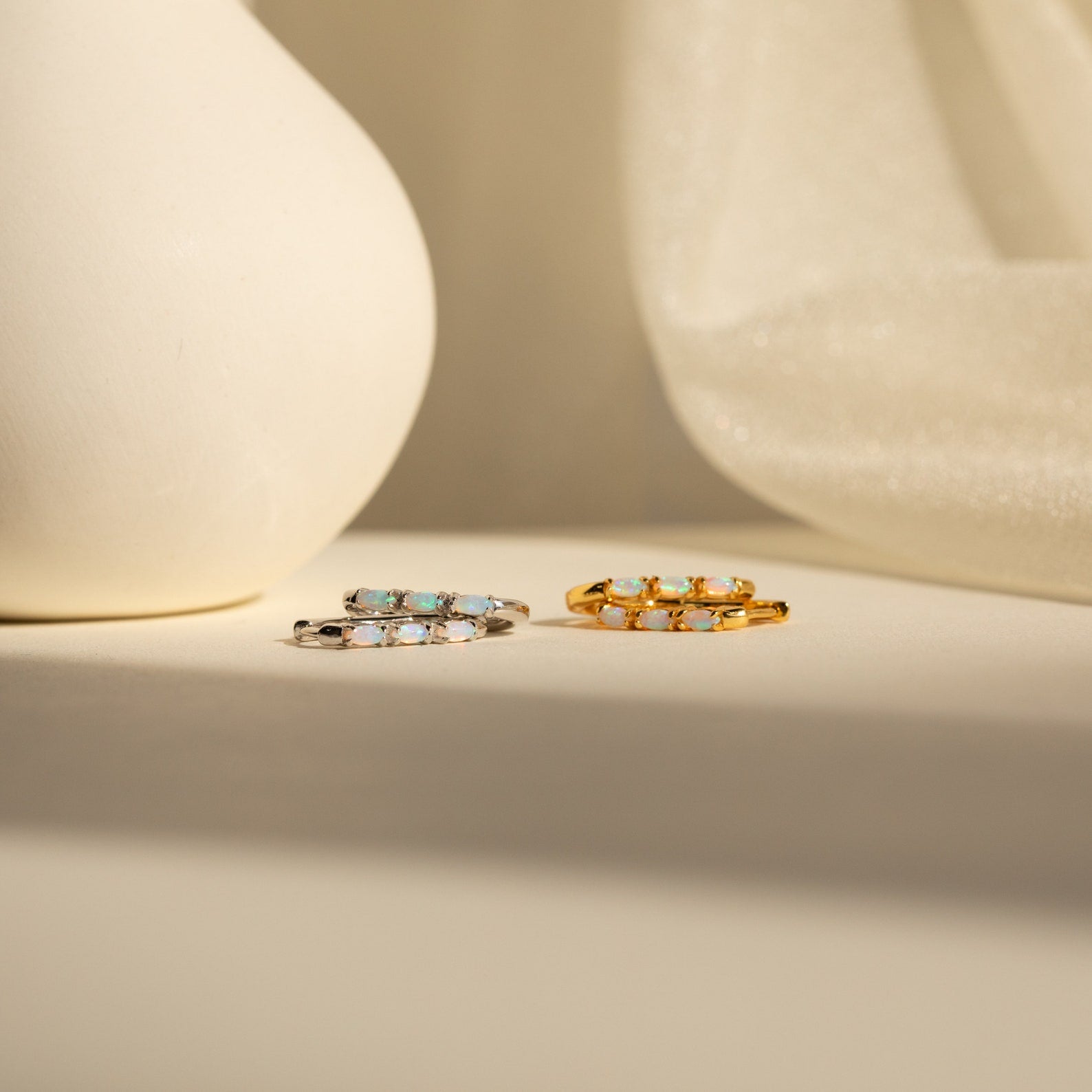 Two gemstone rings—one silver, one gold—rest on a neutral surface with soft lighting, making them the perfect match for your Halo Opal Hoops.