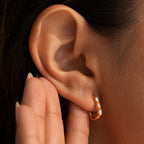 A close-up of an ear wearing minimalist Halo Opal Hoops, with a hand cupped behind the ear.