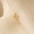 Halo Opal Hoops—gold huggie earrings featuring petite white opals, shown on textured cream fabric for a chic, minimalist style.