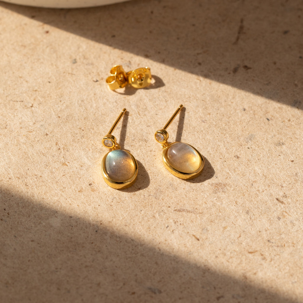 Moonstone Drop Earrings—an elegant set featuring oval, iridescent stones and a small stud pair on a sunlit beige surface, perfect as a minimalist graduation gift.