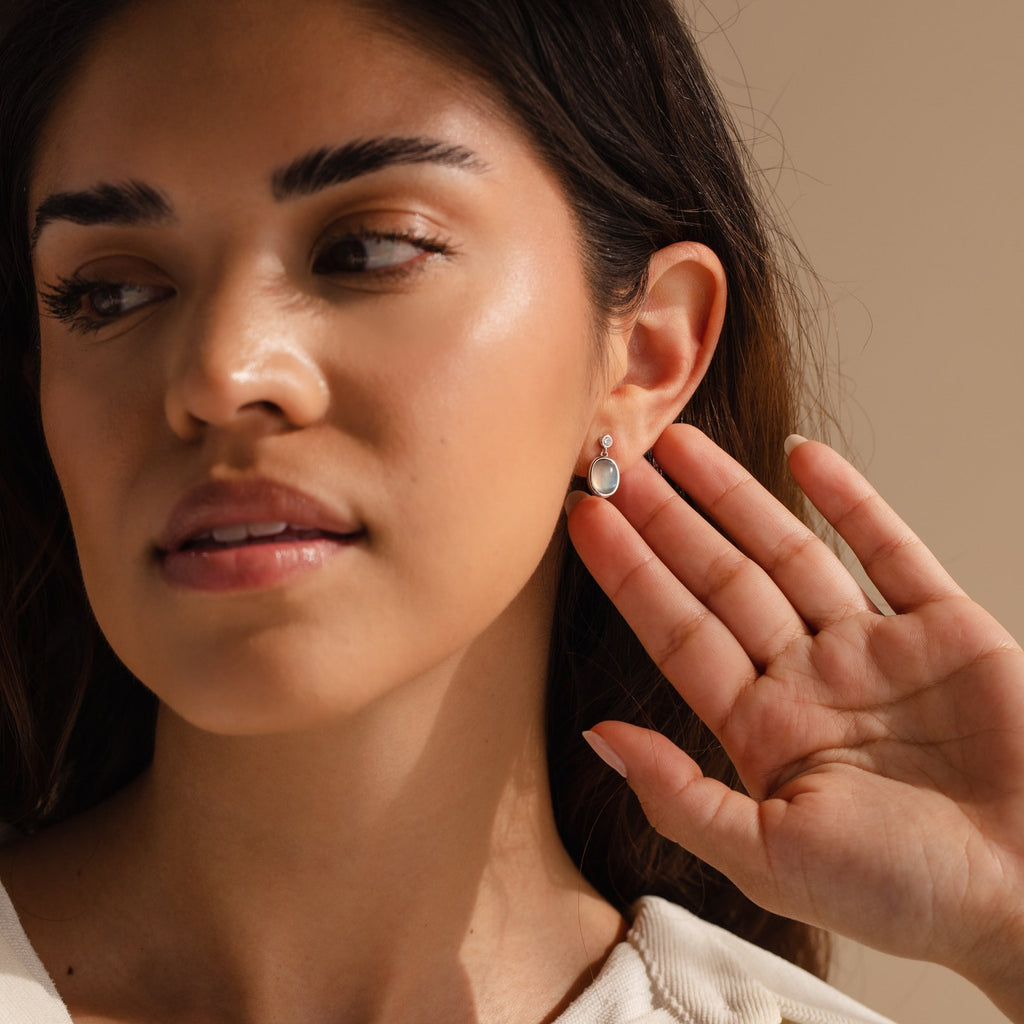 A woman admires her Moonstone Drop Earrings, appreciating their delicate, minimalist design.