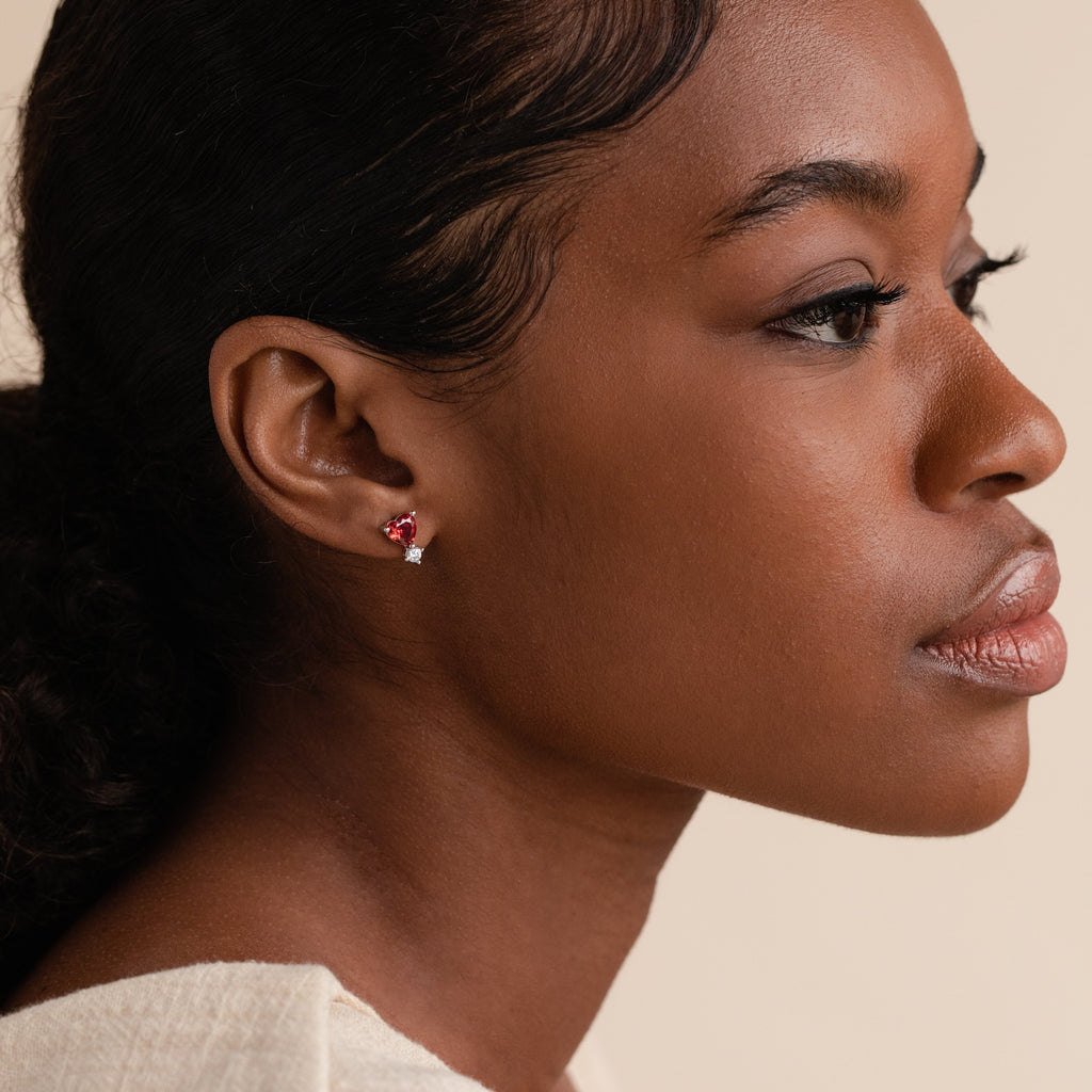 A woman with a ponytail wearing a white shirt and stylish Garnet Heart Studs.