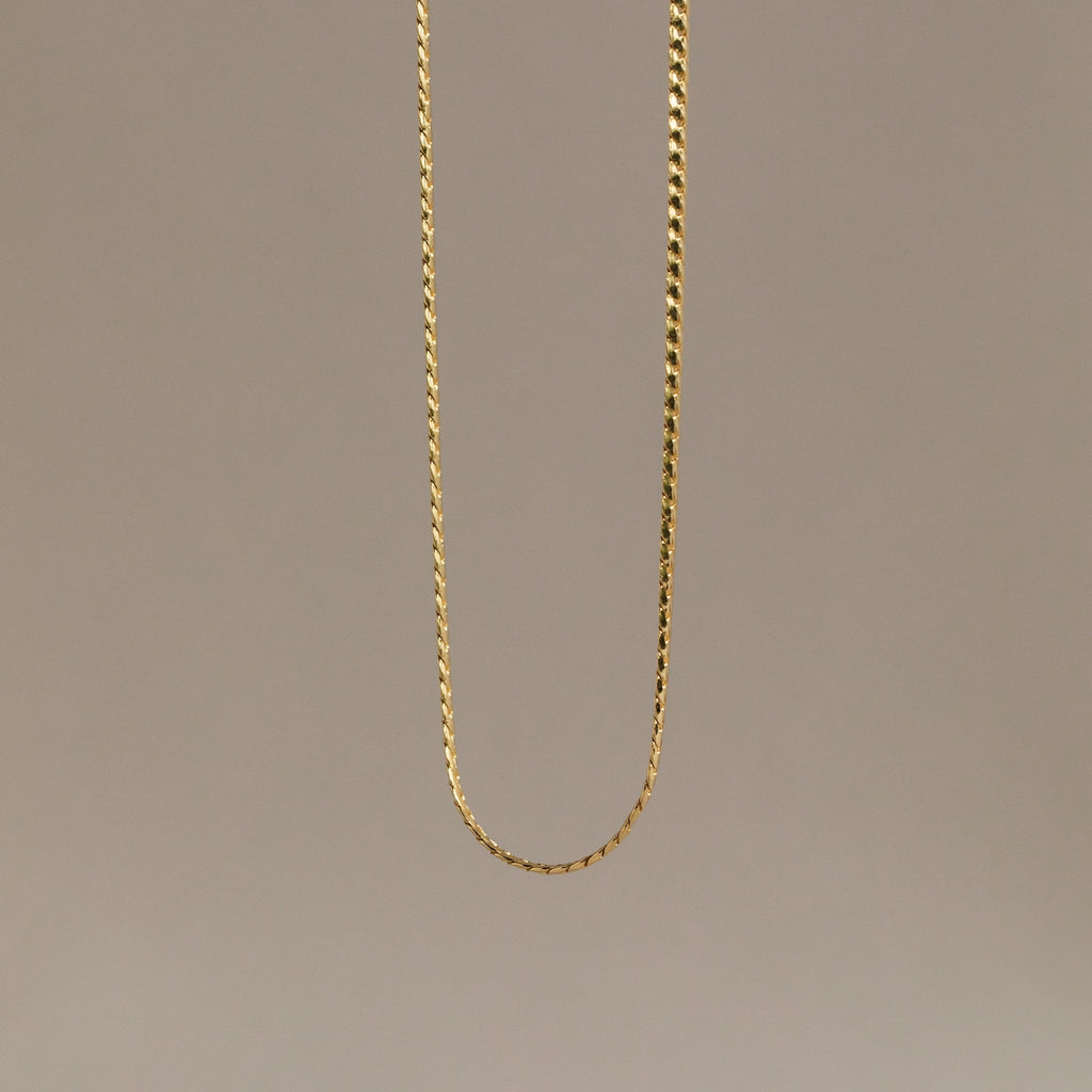 The Men's Snake Chain Necklace hangs against a plain, neutral background, showcasing minimalist elegance and timeless style—an ideal choice for men’s jewelry.