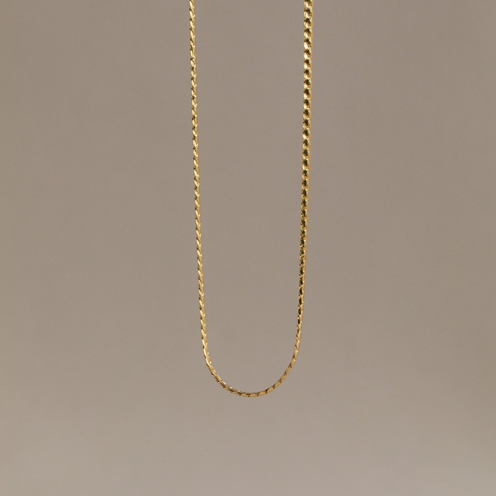 The Men's Snake Chain Necklace hangs against a plain, neutral background, showcasing minimalist elegance and timeless style—an ideal choice for men’s jewelry.