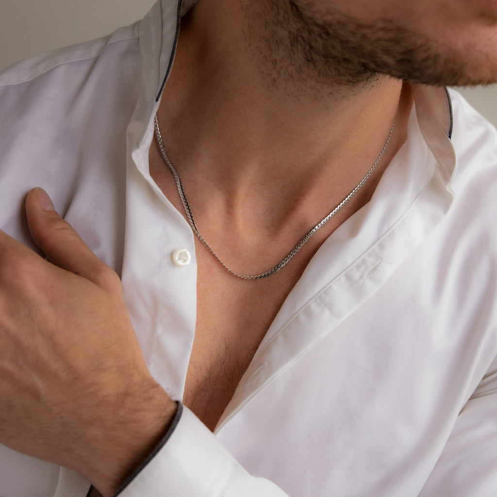 A man in a white shirt wears the Men's Snake Chain Necklace, resting one hand on his chest—a stylish showcase of minimalist men's jewelry.