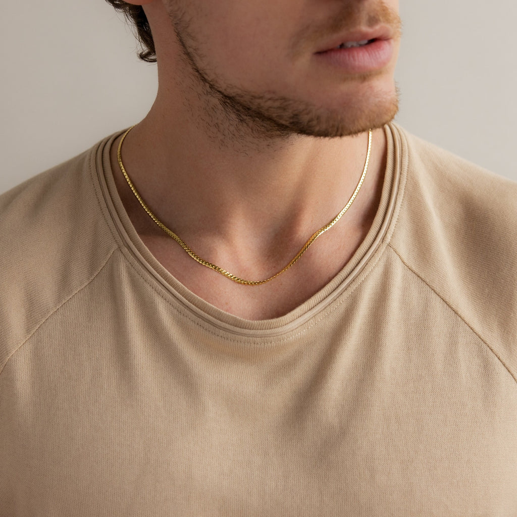 Man wearing a gold herringbone chain necklace, styled with a beige crewneck shirt for a minimal and modern look.
