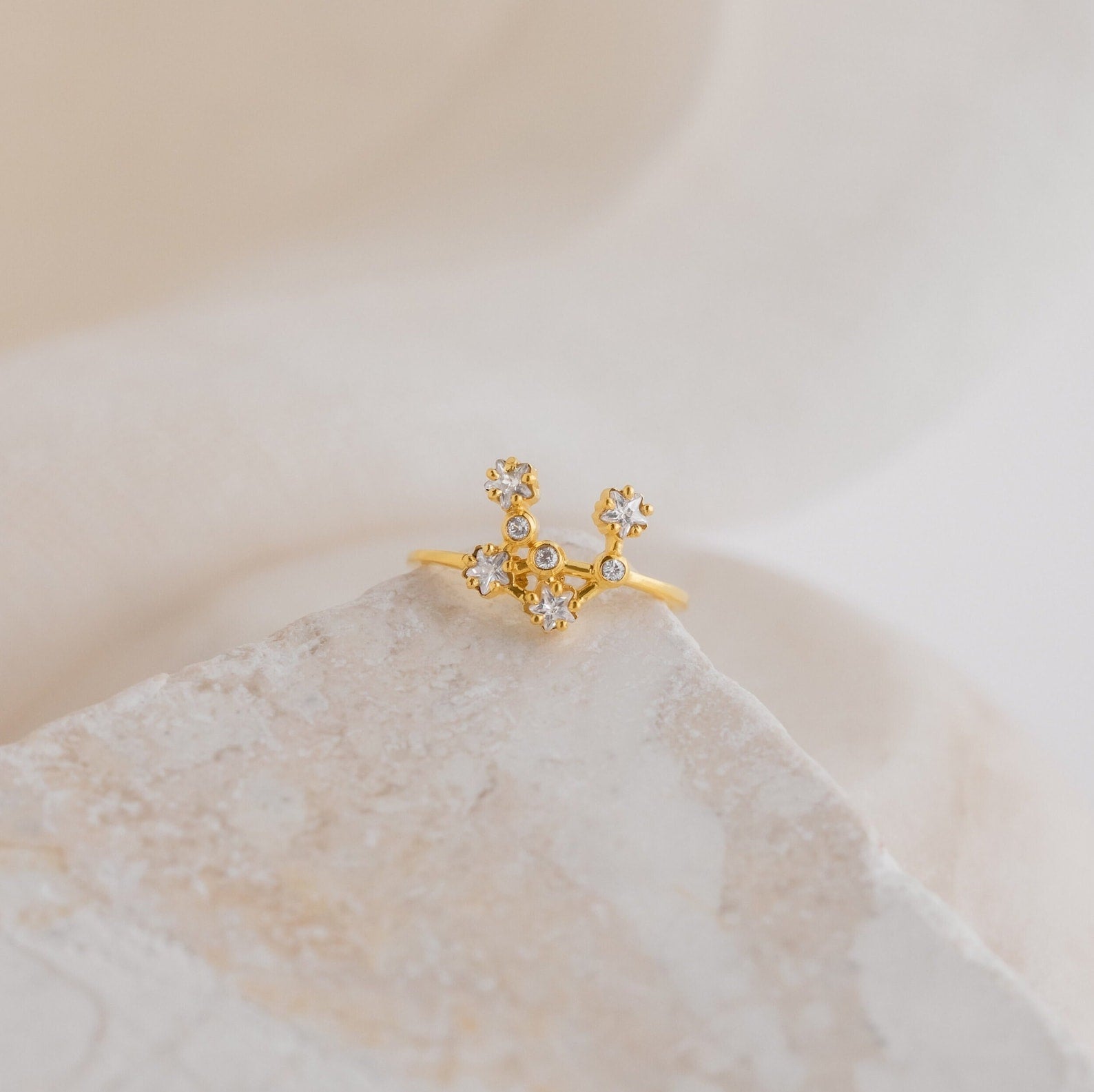 Constellation Ring—an exquisite gold piece with small, sparkling stones in a floral design, displayed on a light textured surface.