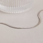 A minimalist necklace, this Men's Snake Chain Necklace is displayed on a light surface beside a textured glass object.