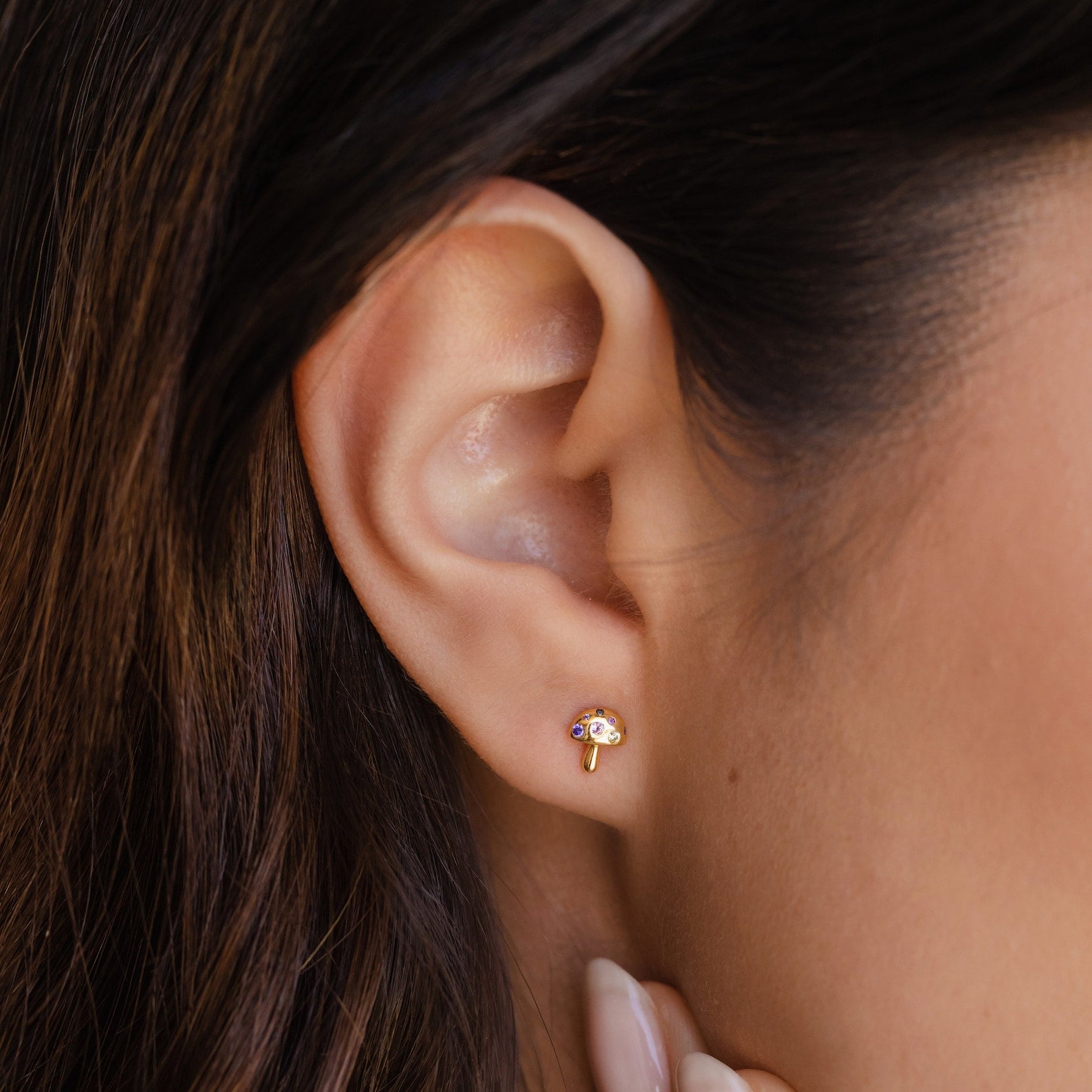 Close-up of a woman's ear wearing Mushroom Studs, gold earrings inspired by nature with colorful accents and sparkling CZ diamonds.