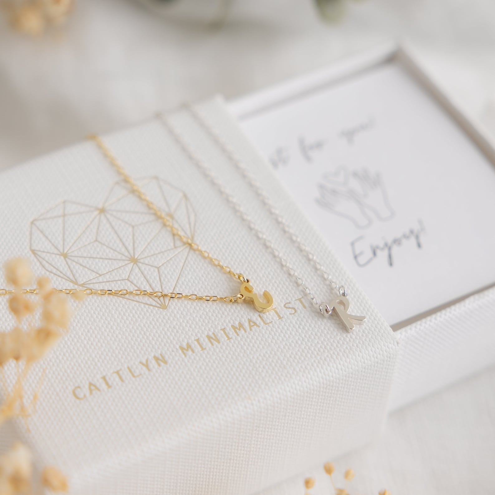 The Stylish Dainty Initial Necklace in gold and silver is beautifully displayed on a textured white box with minimalist packaging—a perfect personalized gift for any occasion.