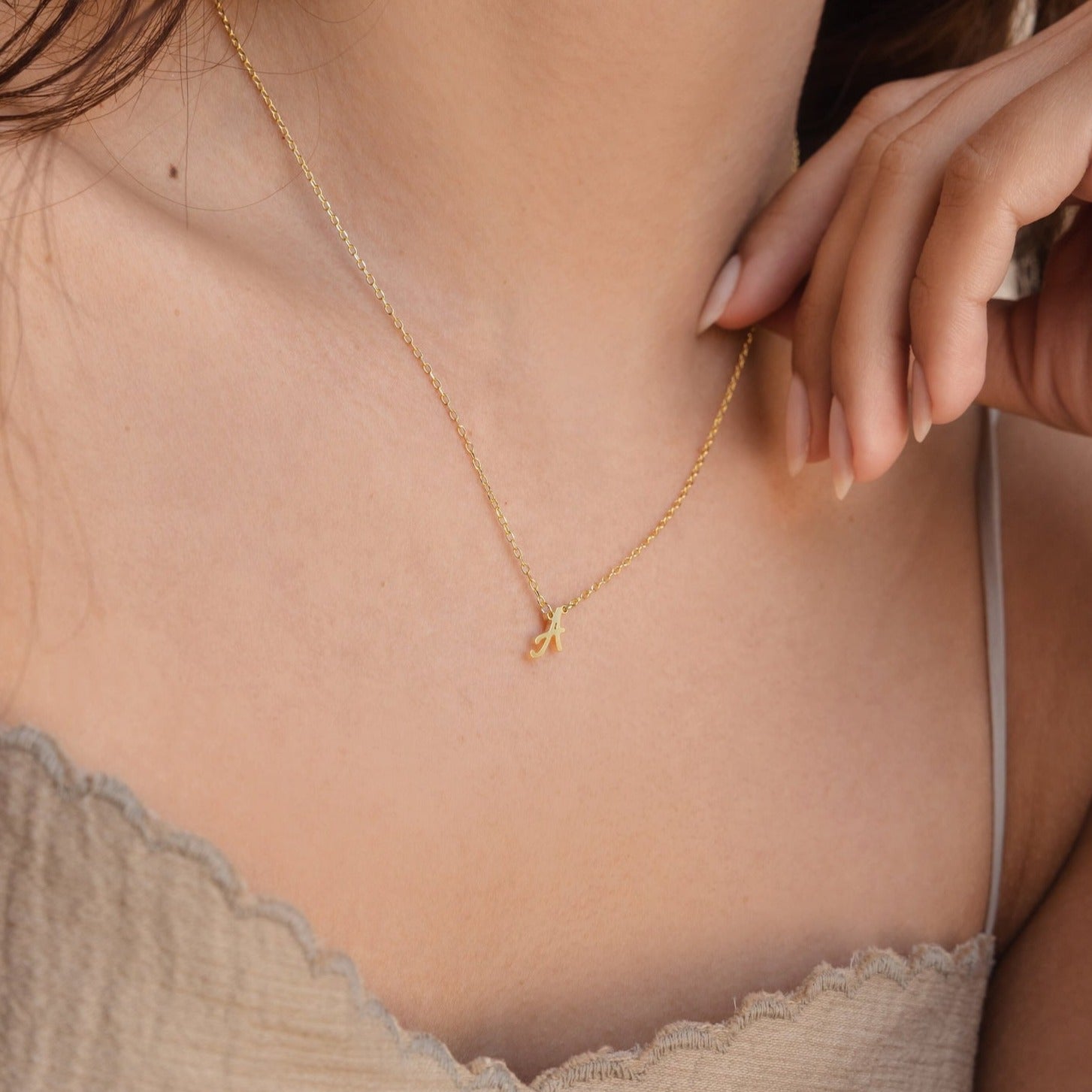 A woman wearing the Grace Dainty Initial Necklace with a small gold letter A pendant gently touches her collarbone.