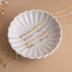 The Tiny Multiple Name Bracelet, ideal for minimal jewelry lovers, is displayed on a white scalloped dish against a beige background.