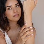 Woman with long hair wears a Tiny Multiple Name Bracelet on her wrist, adding a touch of minimal style to her white sleeveless top.