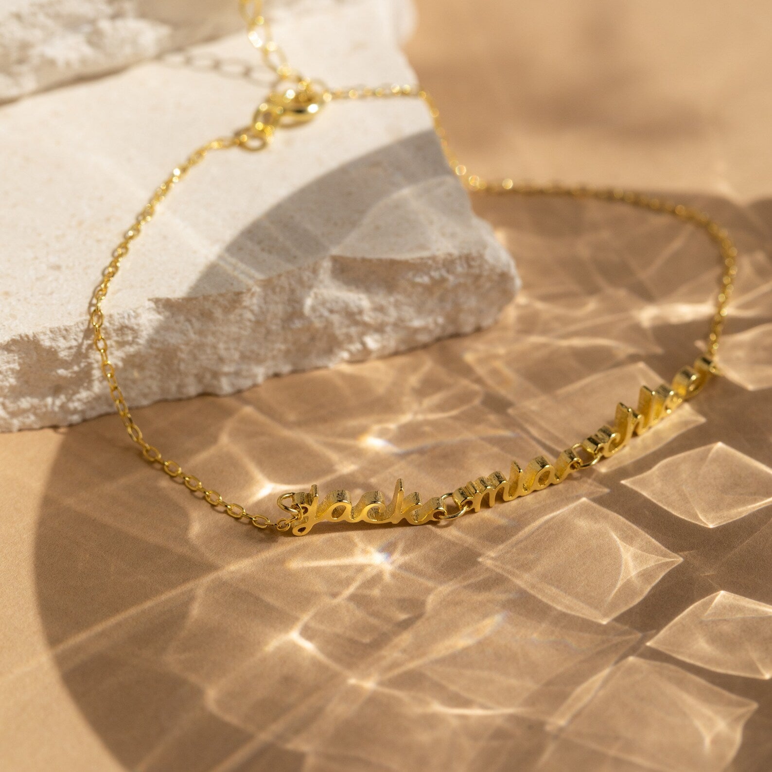 The Petite Tiny Multiple Name Bracelet shines under warm light on textured stone—a perfect minimalist accessory for personalized style.