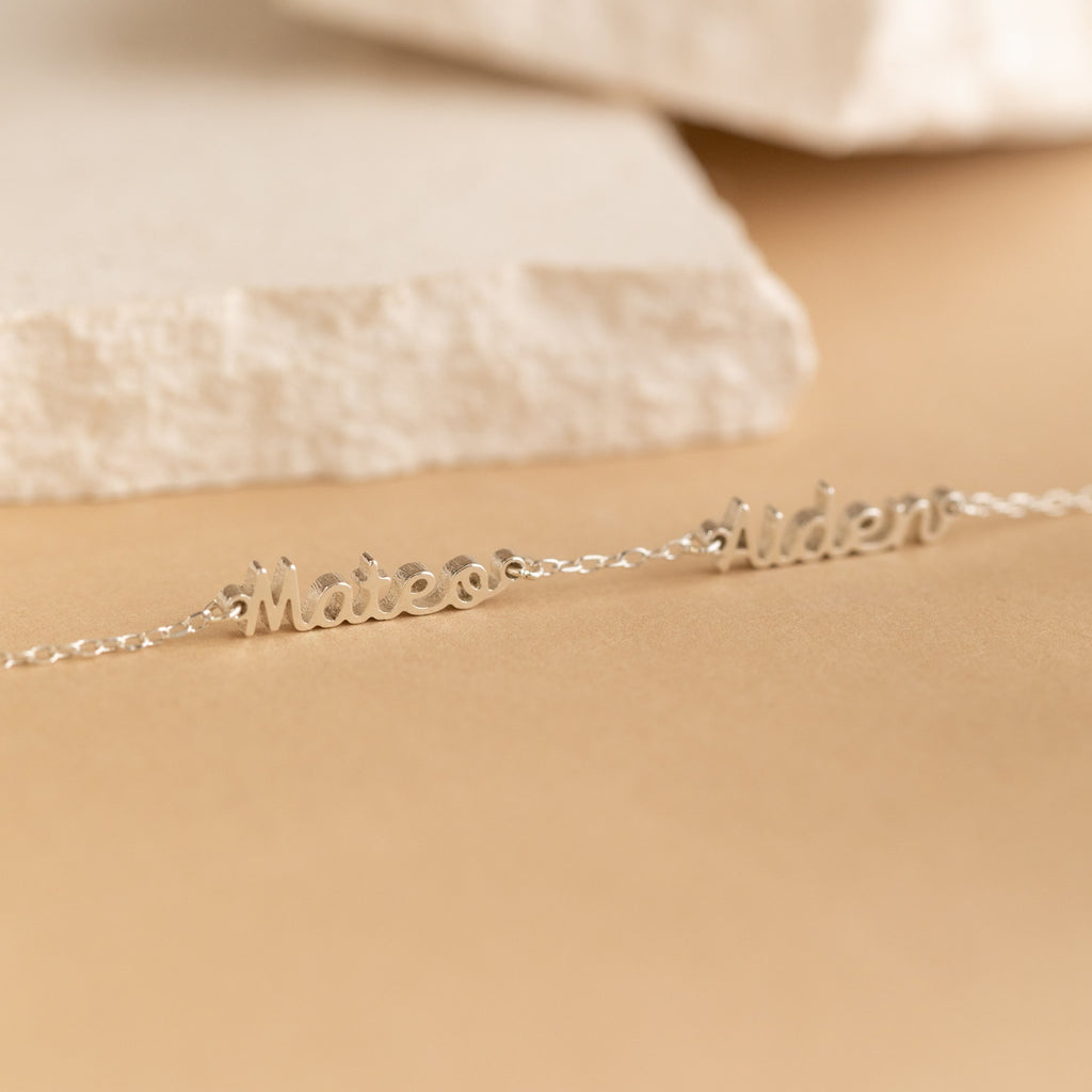 Two silver name necklaces with Mateo and Aiden on a neutral beige surface with a stone background—ideal for pairing with your favorite minimal jewelry or the Petite Tiny Multiple Name Bracelet.