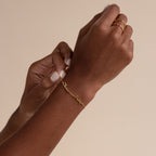 A person wears a Tiny Multiple Name Bracelet and gold rings, showcasing minimal jewelry against a beige background.