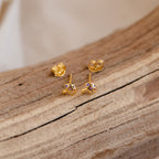 The Mushroom Studs feature gold mushroom-shaped earrings with purple stones, displayed on wood and highlighting elegant, nature-inspired jewelry.