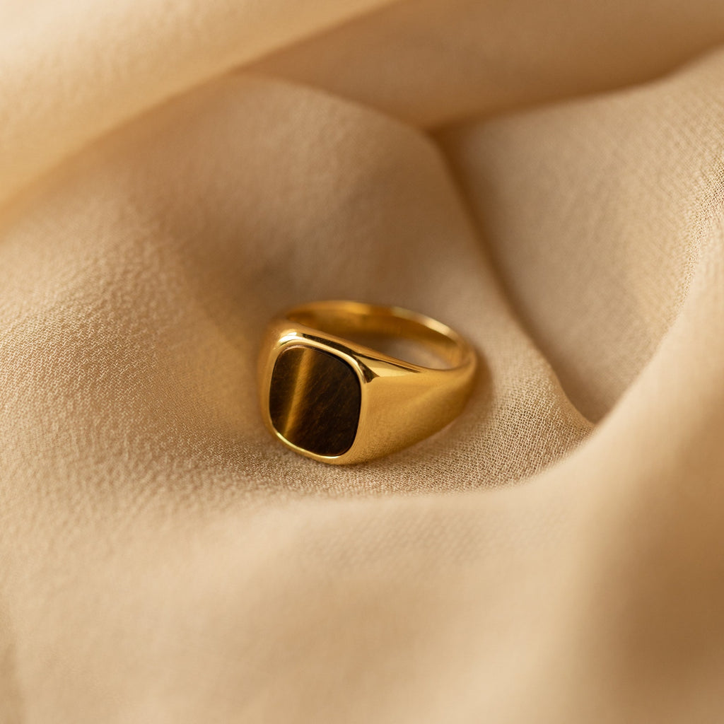 The Tigers Eye Signet Ring in 18K Gold features a striking brown stone and is displayed on soft beige fabric.