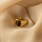 The Tigers Eye Signet Ring in 18K Gold features a striking brown stone and is displayed on soft beige fabric.