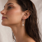 A woman with wet brown hair, shown in profile, wears Pearl Drop Link Studs—statement earrings featuring a silver setting and elegant pearls.