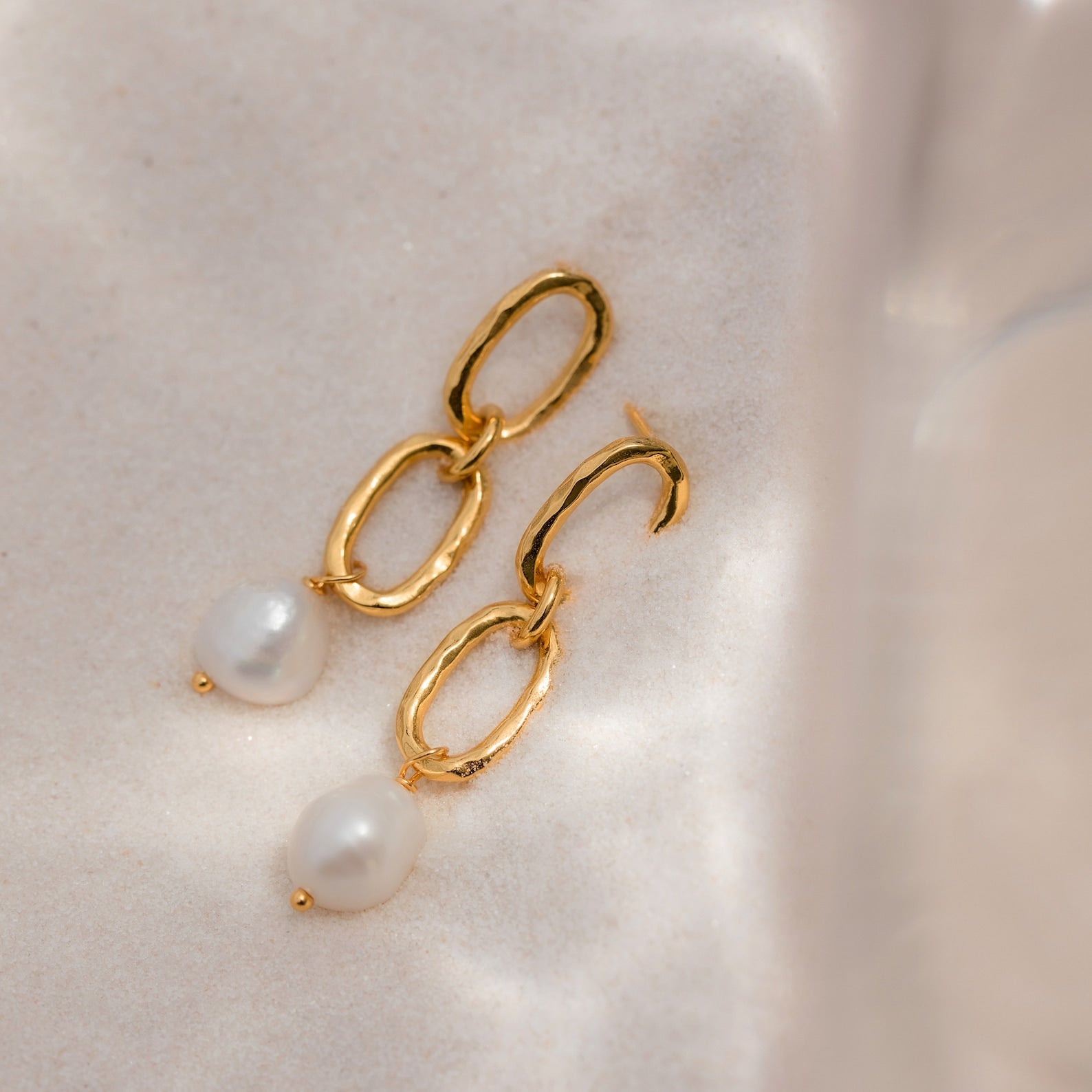 Pearl Drop Link Studs—gold chain link earrings with dangling white pearls, shown on a soft, light fabric background. Elegant pearl drop earrings for a subtle statement.