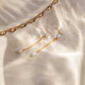 Pearl Drop Chain Earrings featuring white pearls are displayed on sunlit sand next to a glass dish, emphasizing the delicate elegance of this accessory.