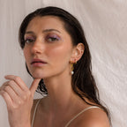 Woman with wet hair, wearing Pearl Drop Link Studs and lavender eyeshadow, poses against a light fabric background.