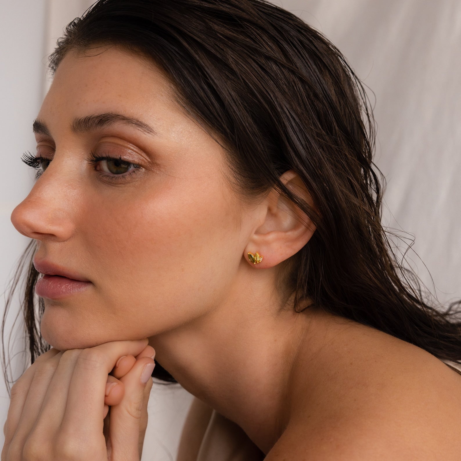 A woman with wet hair rests her chin on her hands, wearing Seagrass Peridot Marquise Studs, against a neutral background.
