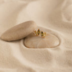 Seagrass Peridot Marquise Studs showcased on smooth stones nestled in soft sand.