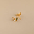 Seagrass Peridot Marquise Studs: Gold stud earrings with marquise and round-cut peridot stones add elegant sparkle against a beige backdrop.