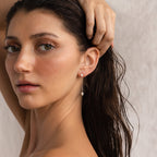 A woman with wet hair tucks it behind her ear, highlighting the Pearl Drop Chain Earrings against a neutral background.