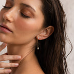 A woman with wet hair, eyes closed, gently touches her chin while wearing Pearl Drop Chain Earrings.